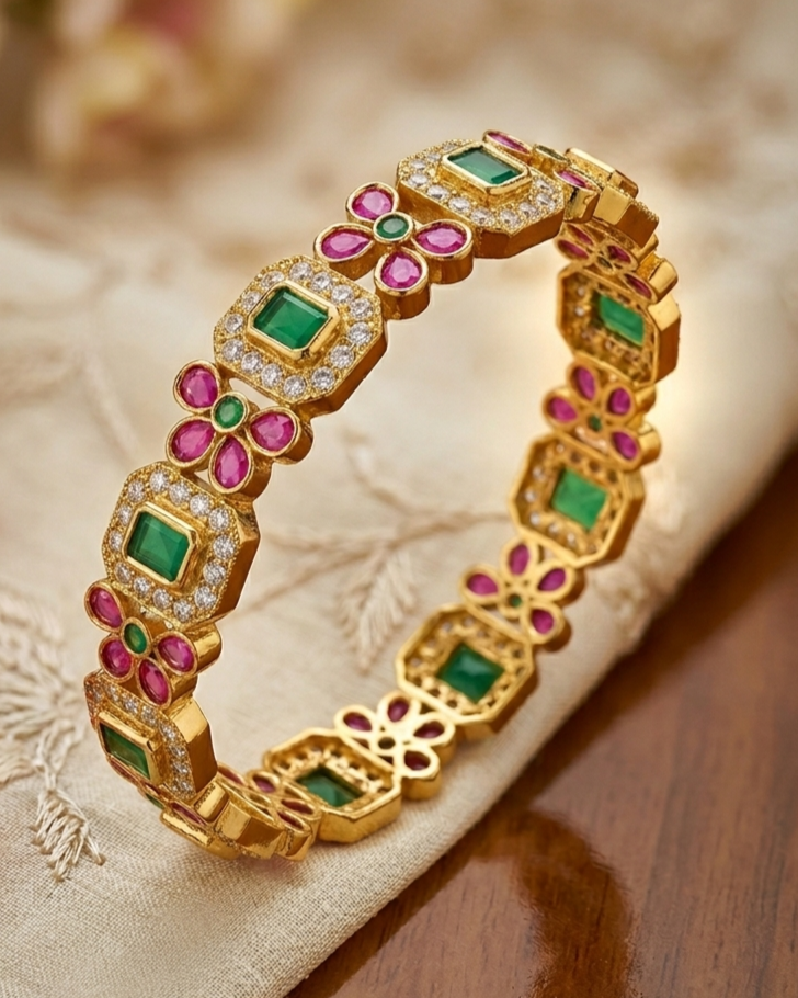 Gold bracelet with green and pink gemstones on a textured surface