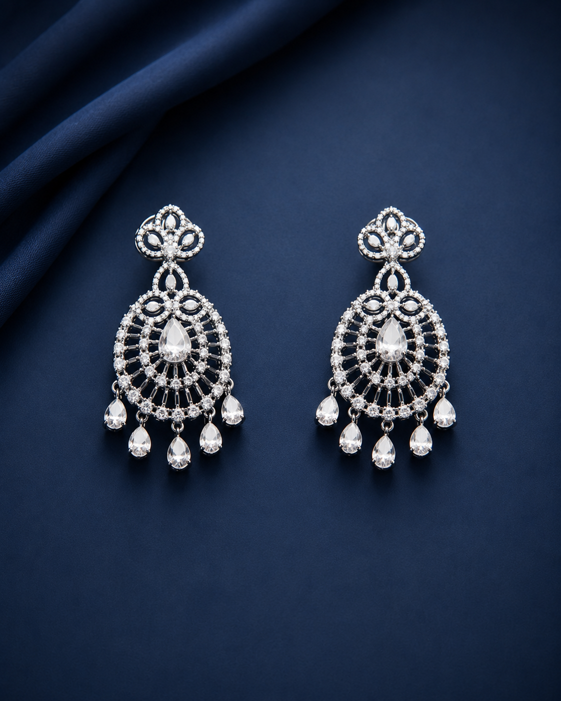 Ornate silver earrings with clear stones on a dark blue fabric background