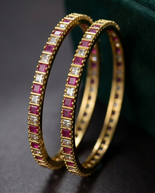 Gold bangles with red and white stones on a dark surface