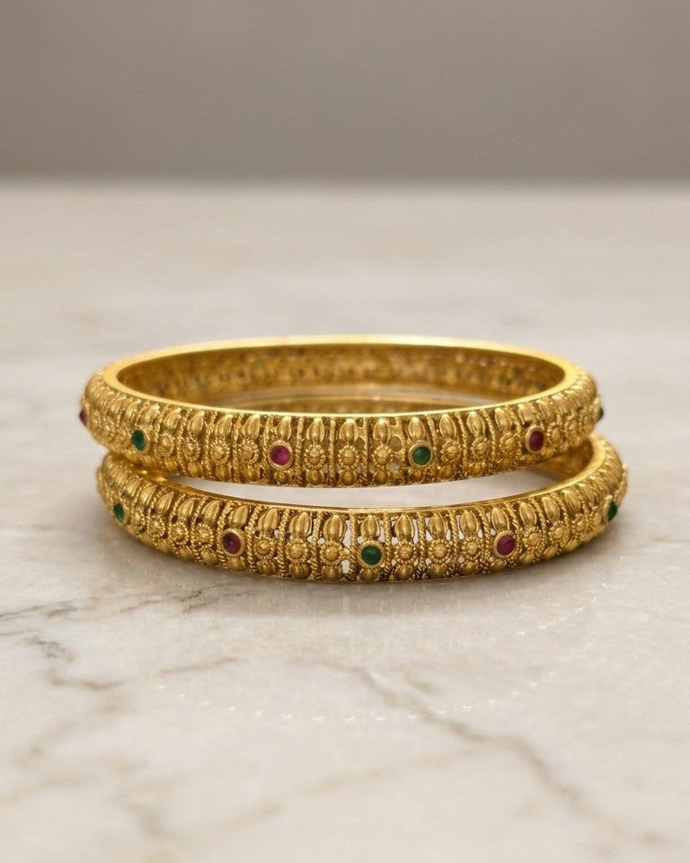 Two gold bangles with embedded gemstones on a marble surface