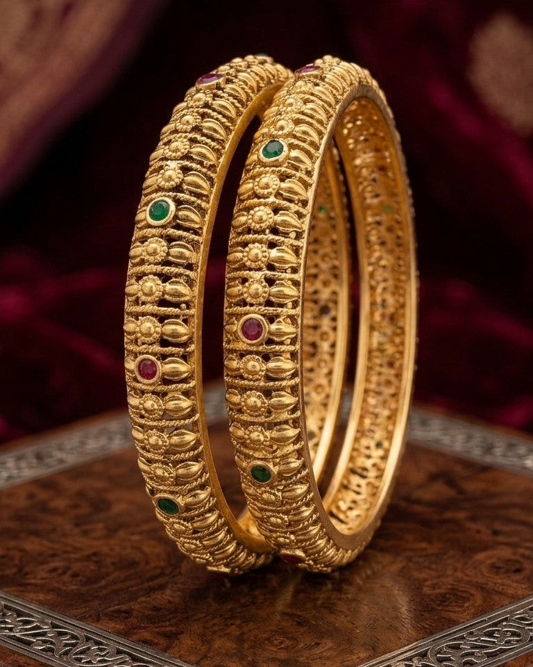 Two gold bangles with gemstones on a dark background