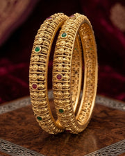 Two gold bangles with gemstones on a dark background