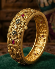 Gold bracelet with intricate designs and red gemstones on a green surface