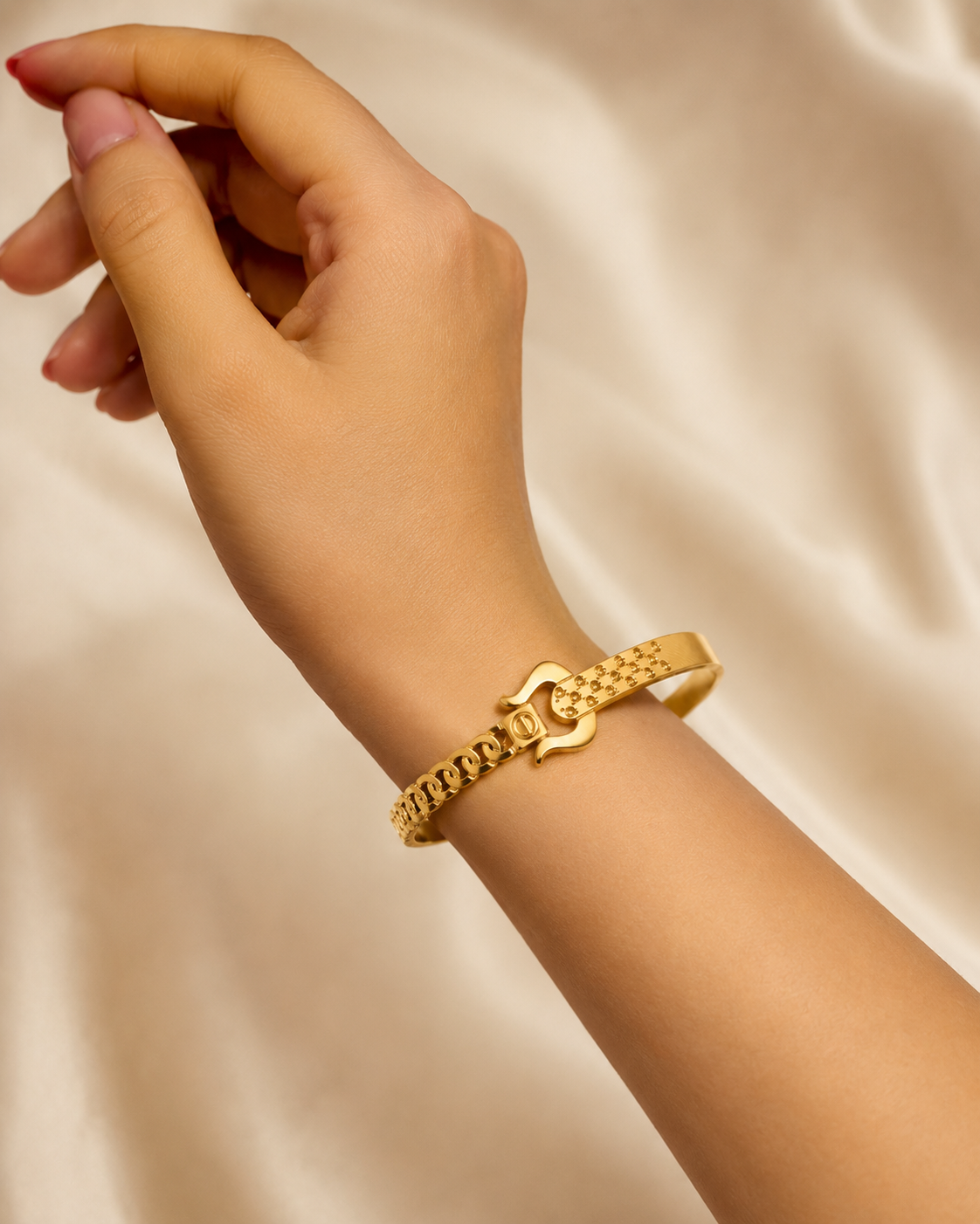 A gold-tone chain bracelet with a decorative interlocking ring clasp, shown worn on a person's wrist against a soft beige satin background.
