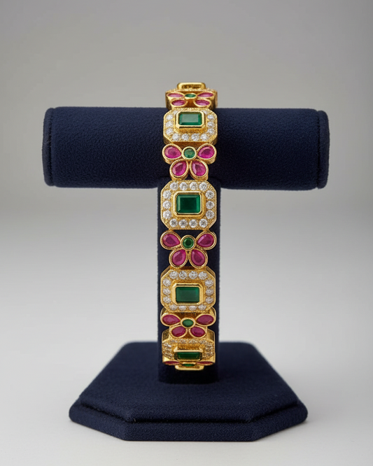 Gold bracelet with green and pink gemstones on a textured surface