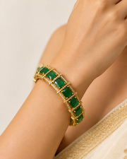 Gold bracelet with green gemstones on a green stand against a white background