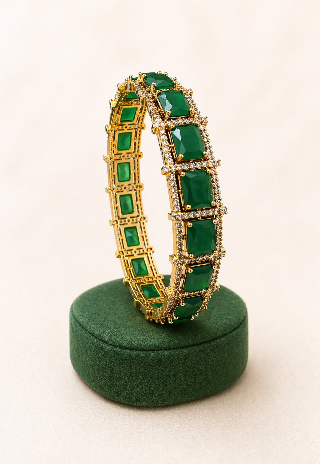 Gold bracelet with green gemstones on a green stand against a white background