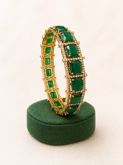Gold bracelet with green gemstones on a green stand against a white background