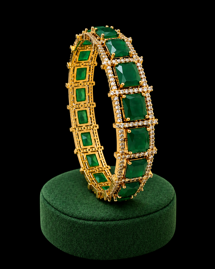 Gold bracelet with green gemstones on a green stand against a white background