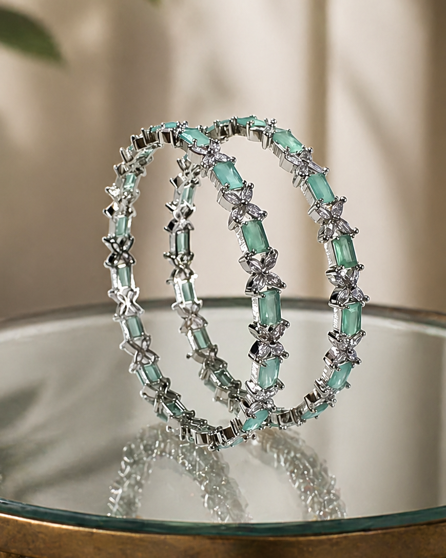 Three silver-toned bangles with mint green rectangular and star-shaped stones, displayed on a reflective glass surface.
