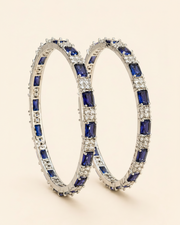 Pair of hoop earrings with blue gemstones and clear stones on a beige background