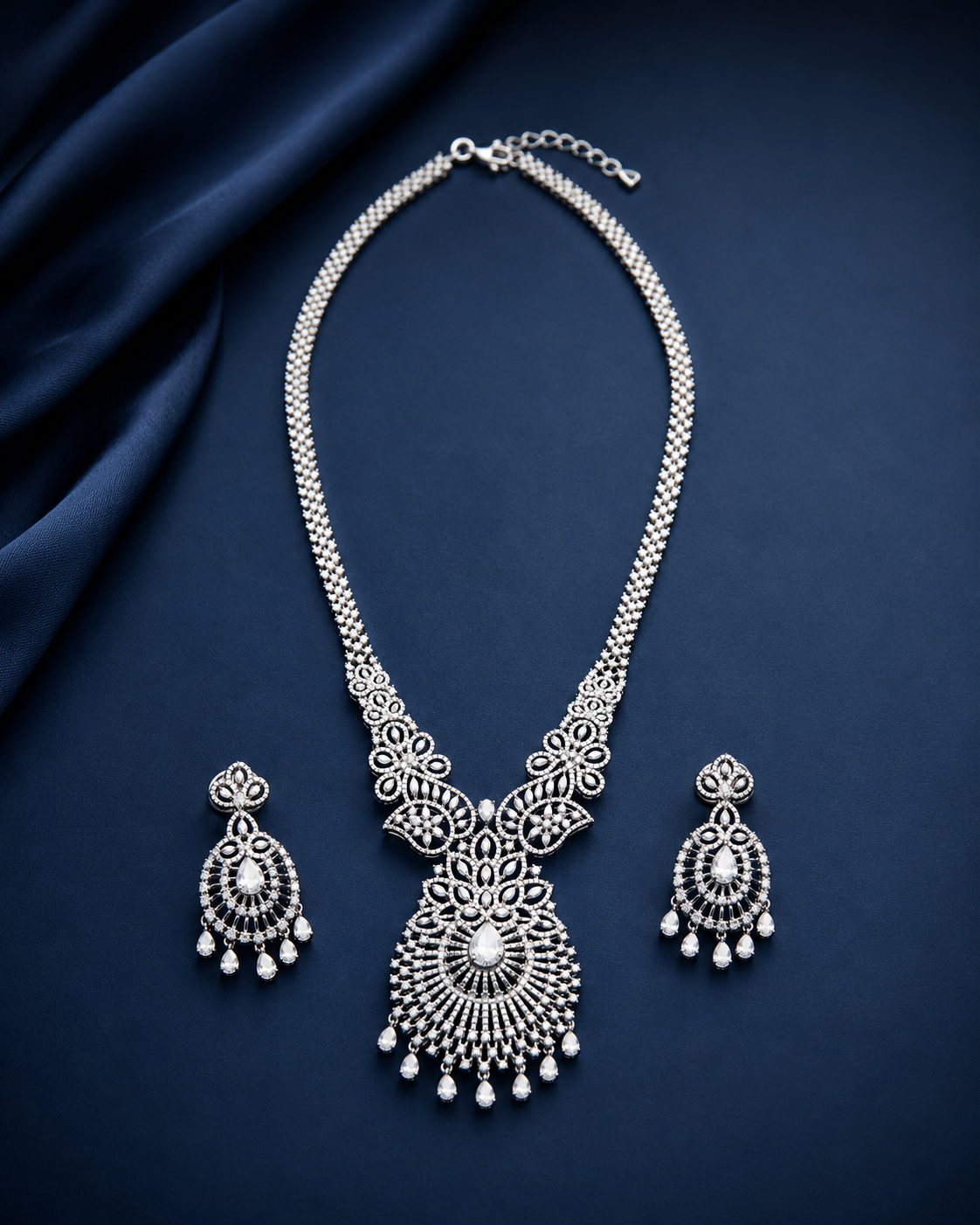 Silver necklace and earrings set on a dark blue fabric background