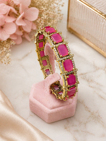 Pink and gold hoop earrings on a pink cushion with flowers and a box in the background