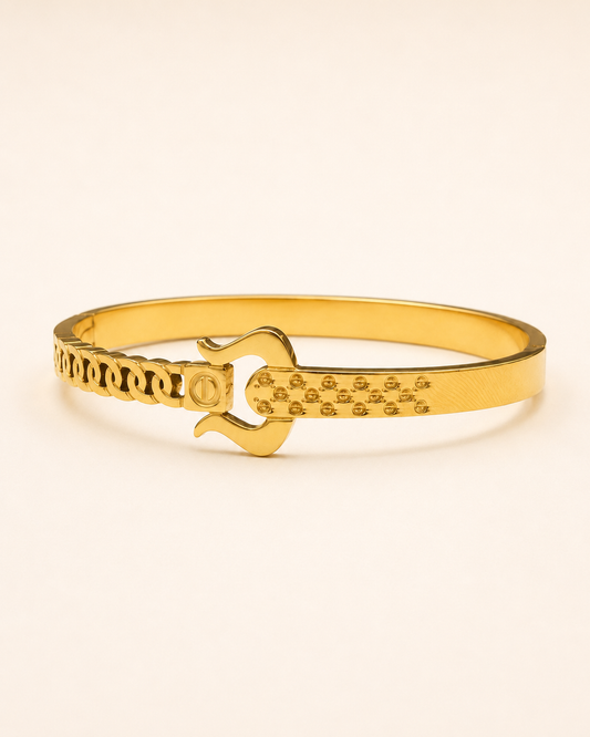 A gold-plated bangle bracelet featuring a central lock pick design and textured patterns on its ends, set against a plain off-white background.