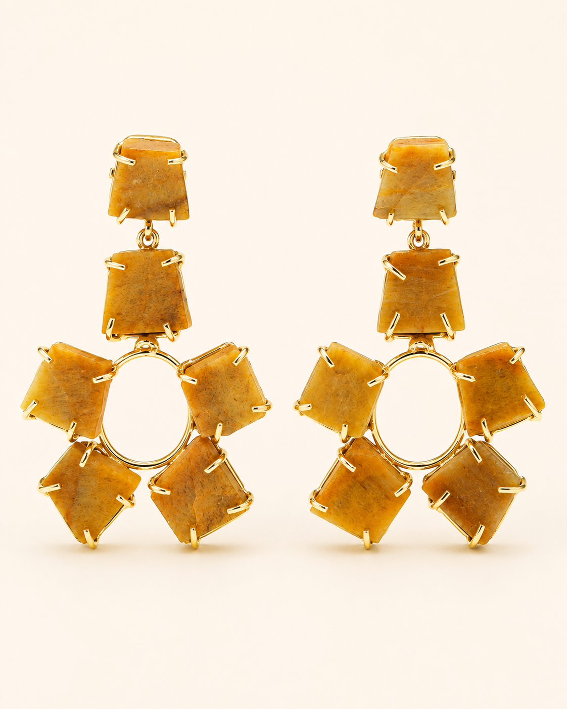 A pair of gold drop earrings featuring a central circular gold ring surrounded by six faceted, stepped amber-yellow stones, with three matching stones stacked vertically above the center, set against a plain cream background.