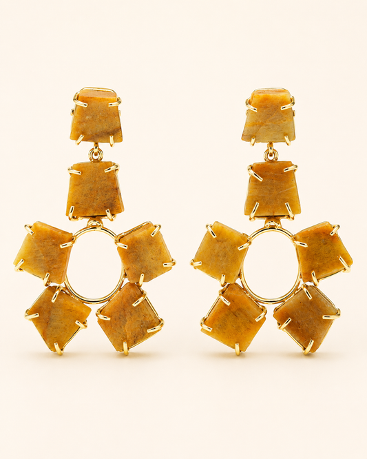 A pair of gold drop earrings featuring a central circular gold ring surrounded by six faceted, stepped amber-yellow stones, with three matching stones stacked vertically above the center, set against a plain cream background.