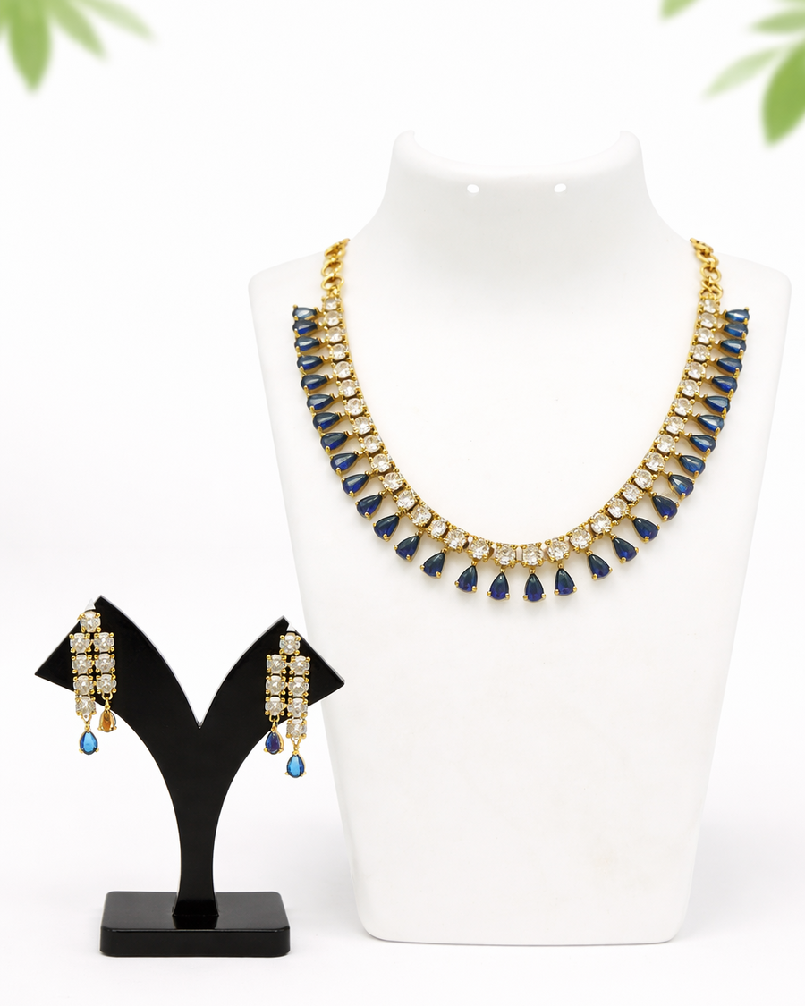 Gold necklace with green stones on a white bust beside matching earrings on a black stand