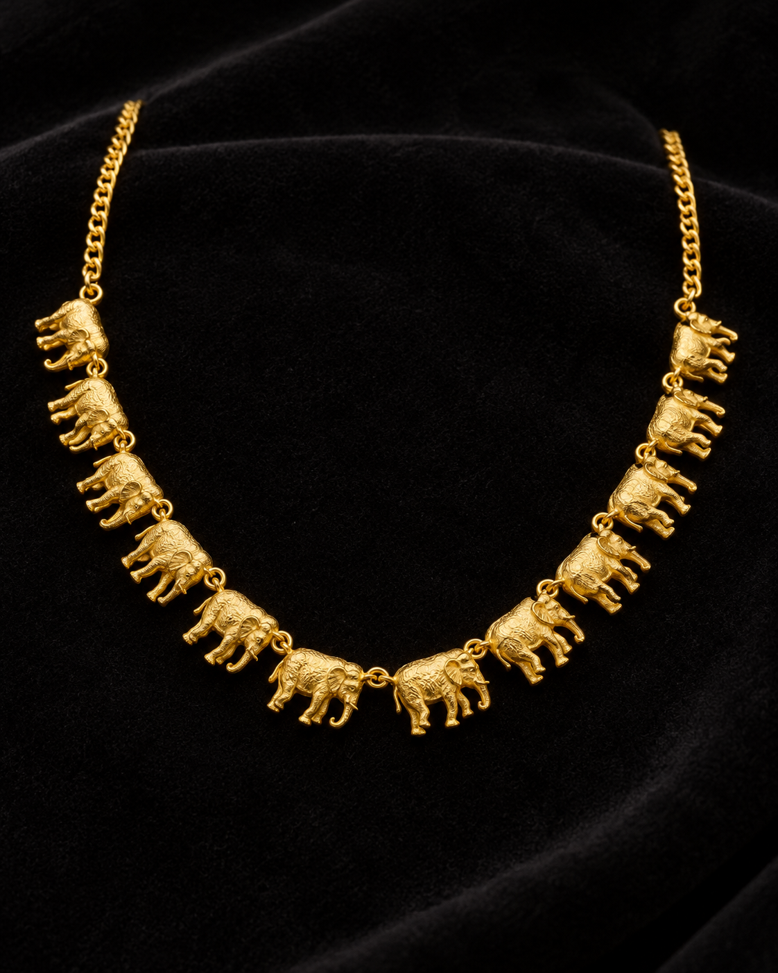 A gold chain necklace featuring a series of small elephant charms, displayed on a black velvet background.