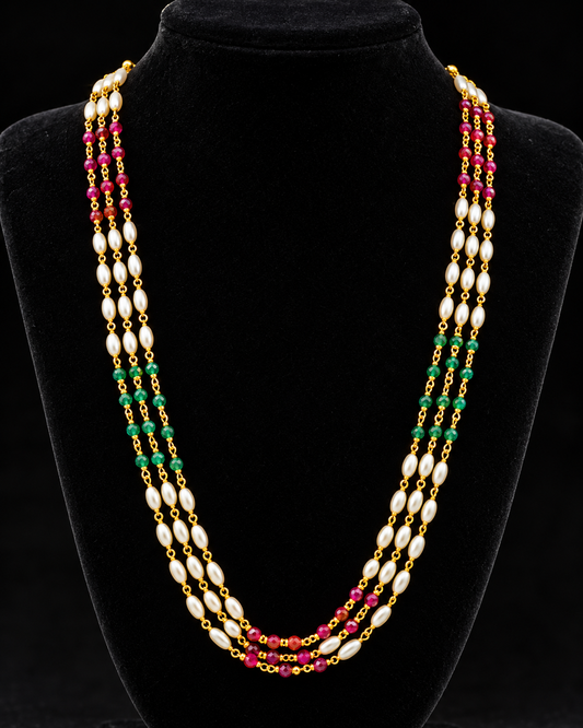 A multi-strand pearl necklace with gold-toned beads and alternating green and pink gemstone accents, displayed on a black velvet jewelry bust against a black background.
