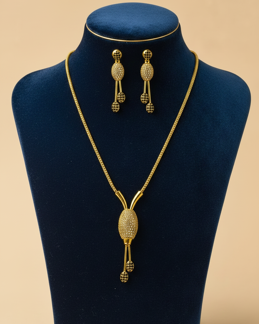 Gold jewelry set featuring a necklace and matching earrings displayed on a dark teal jewelry bust against a warm beige background.