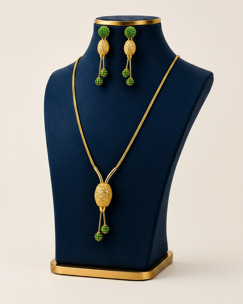 Gold jewellery set featuring a pendant necklace and matching drop earrings displayed on a dark blue jewellery bust against a light beige background.