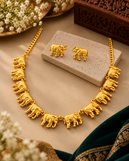 Gold elephant necklace and matching stud earrings displayed on a beige stone block, with decorative flowers and a carved wooden box in the background.