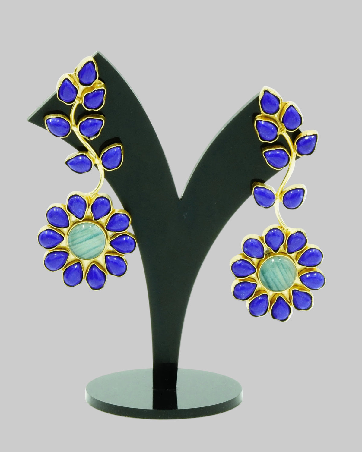 A pair of gold and blue enamel flower earrings displayed on a black V-shaped jewelry stand against a white background.
