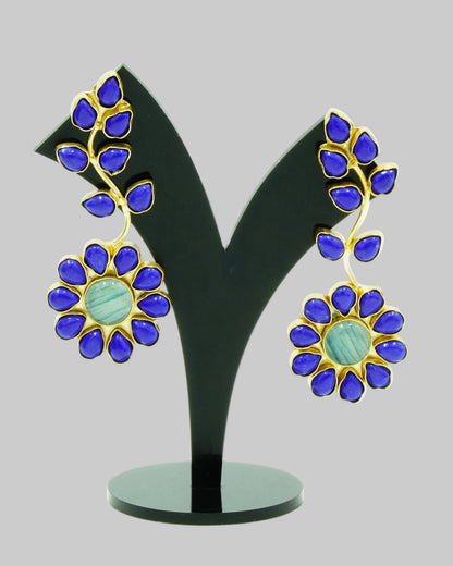 A pair of gold and blue enamel flower earrings displayed on a black V-shaped jewelry stand against a white background.