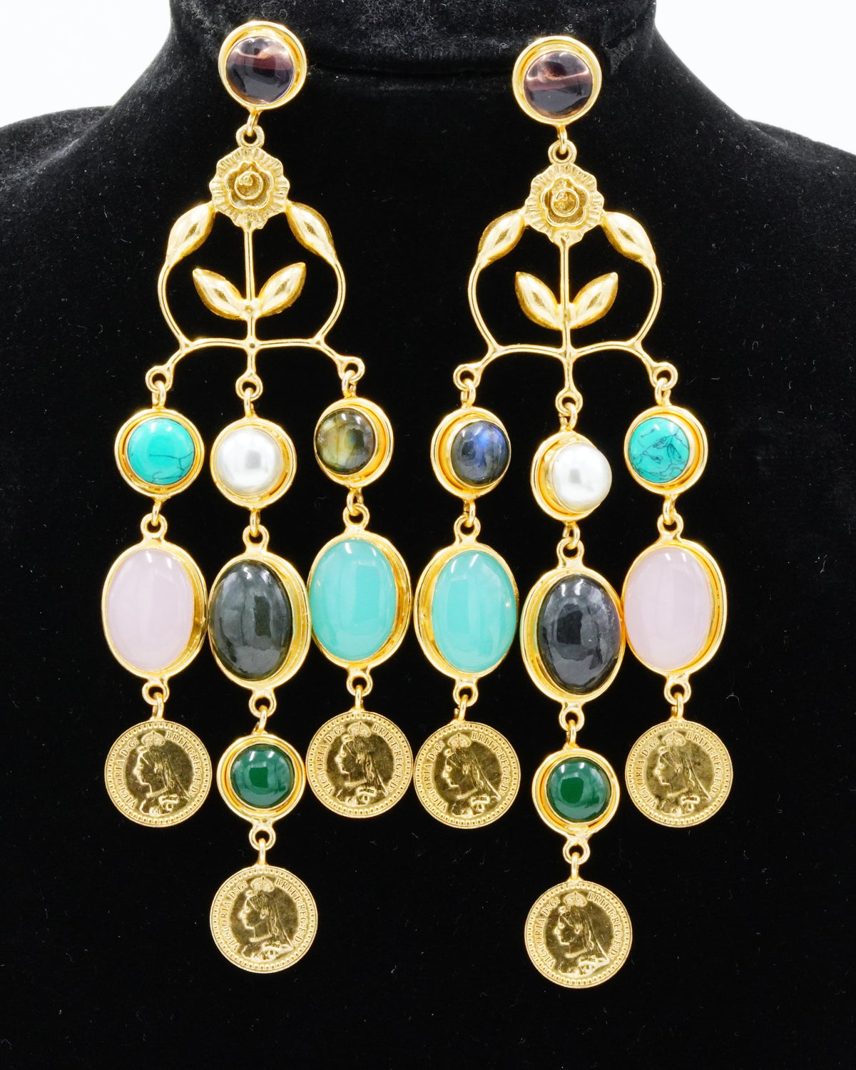 A pair of gold-toned statement dangle earrings displayed on a black velvet jewelry bust against a white background. The earrings feature multiple colorful gemstone drops including turquoise, white, pink, green, and dark gray, with round gold coin-like charms at the bottom.