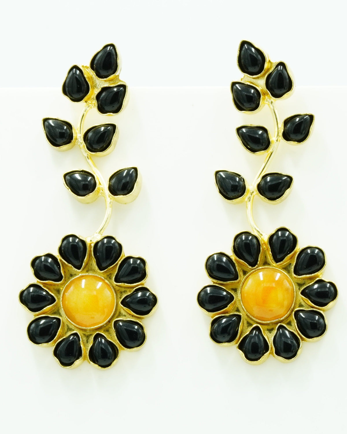 A pair of gold and black dangle earrings featuring a floral design with a central round amber-yellow stone surrounded by black teardrop-shaped stones, with leafy vine details above, set against a plain white background.