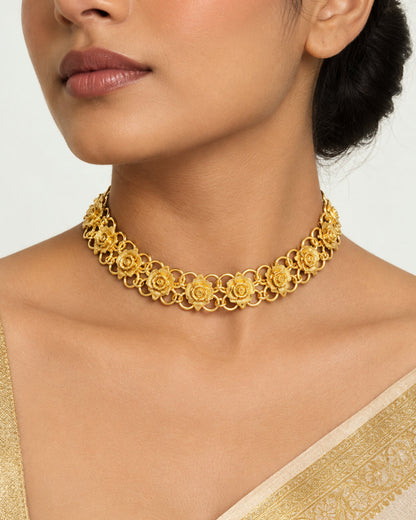 A gold-tone floral link chain necklace displayed on a black velvet jewelry bust against a light gray background.