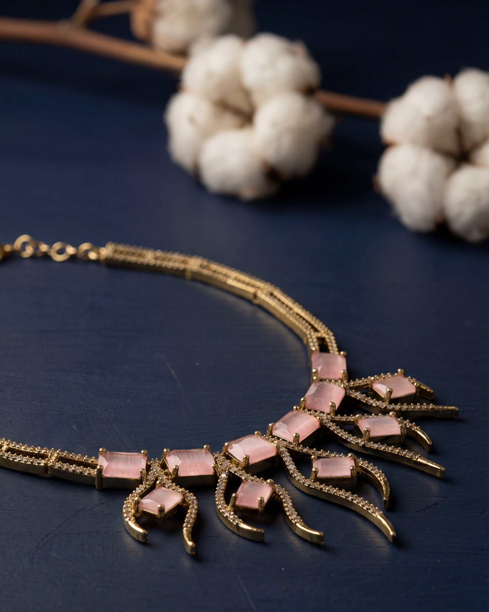 Gold necklace with pink stones on a dark surface with white flowers in the background