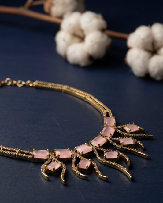 Gold necklace with pink stones on a dark surface with white flowers in the background