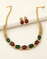 Gold-tone necklace and matching stud earrings set with oval red and green gemstones and small clear rhinestone accents, displayed on a cream background.