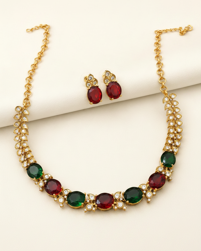 Gold-tone necklace and matching stud earrings set with oval red and green gemstones and small clear rhinestone accents, displayed on a cream background.