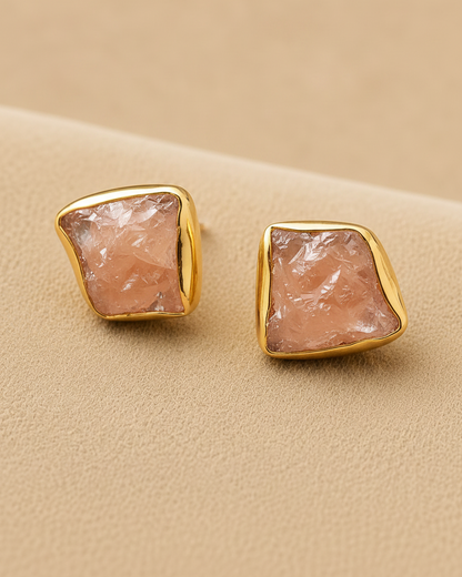 Gold earrings with pink stone on a beige background