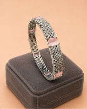 Silver bracelet with pink accents on a gray cushion against a beige background