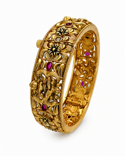Gold bracelet with intricate designs and red gemstones on a white background