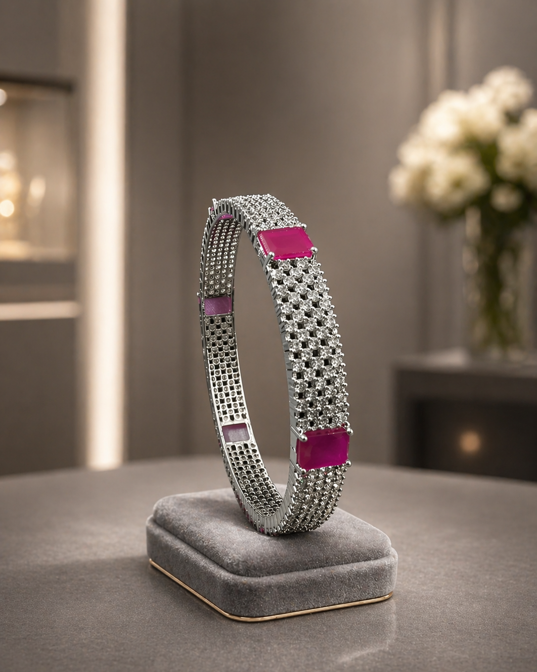 Silver bracelet with pink accents on a gray stand against a neutral background