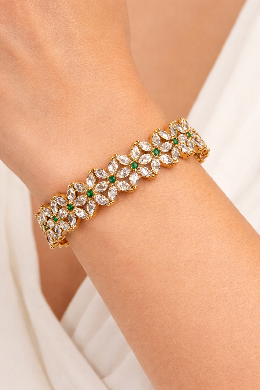 Gold bracelet with gemstones on a person's wrist against a neutral background