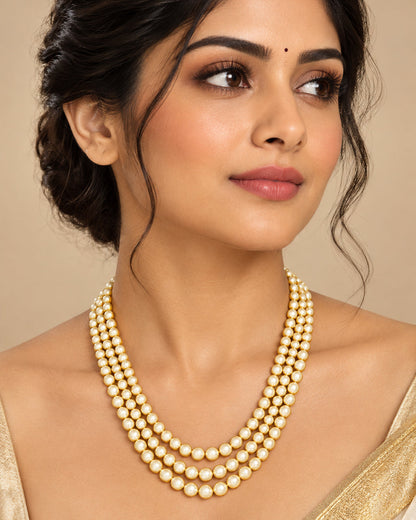 A gold and pearl jewelry set displayed on a black velvet mannequin bust, featuring a multi-strand pearl necklace and matching drop earrings on a light gray background.