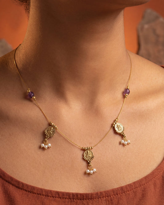 Necklace with floral designs and beads on a person wearing a rust-colored top against an orange background