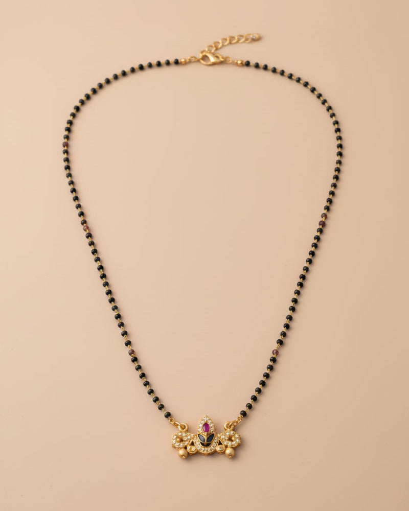 Black bead mangalsutra with a gold Balaji idol pendant on a beige background