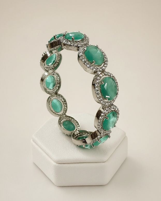 Bracelet with green gemstones on a white stand against a beige background